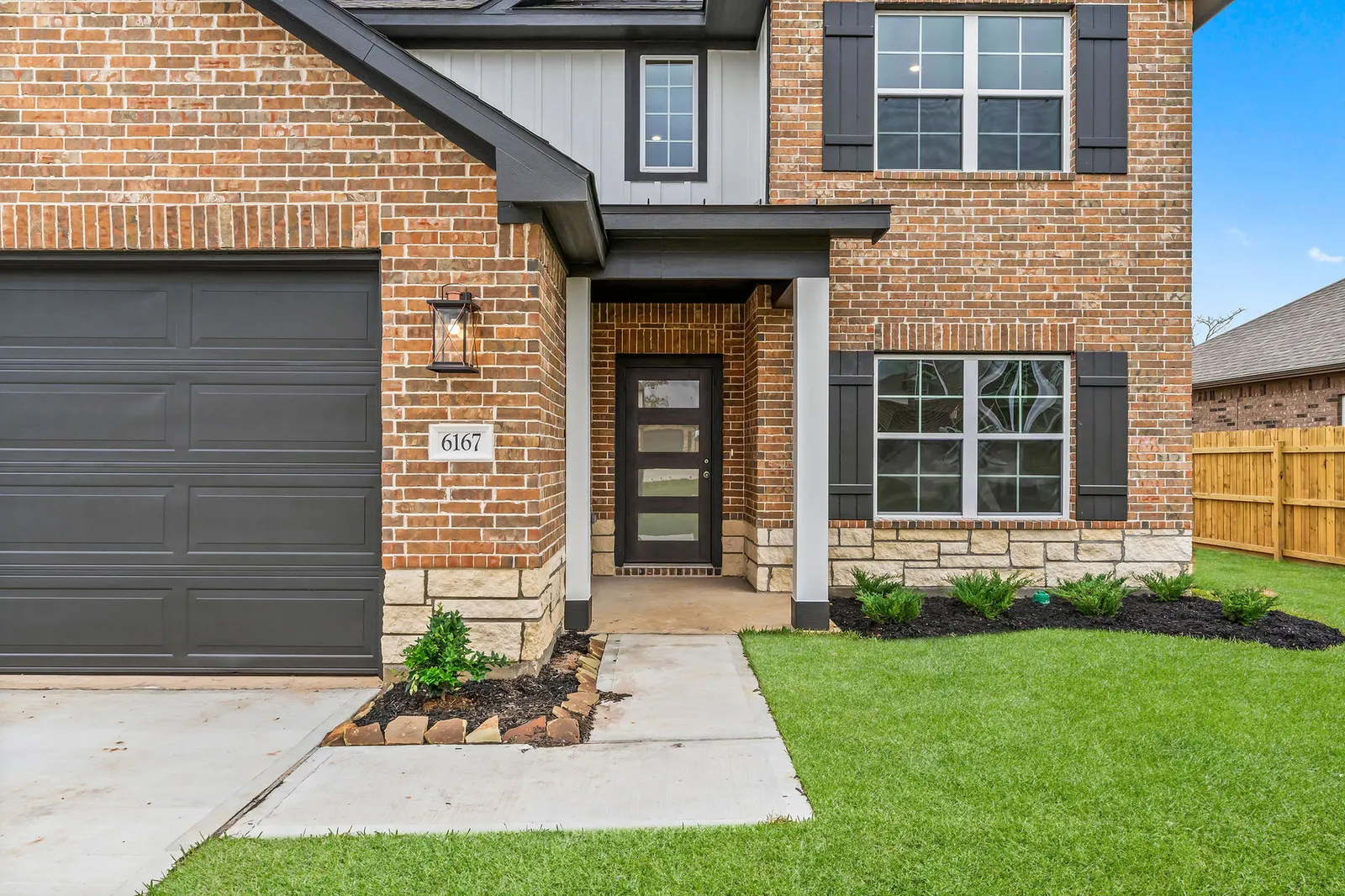 Front entry and garage of a two story Alta home, brick with dark shutters and a landscaped lawn